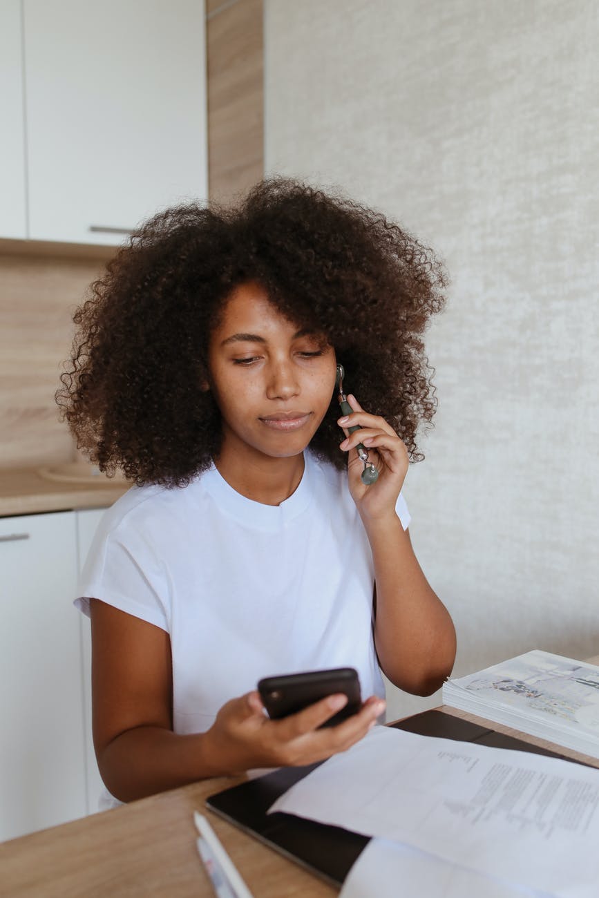 a woman massaging her face with a jade roller while browsing her smartphone